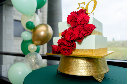 A festive cake of 50th anniversary with red roses and golden strips and colorful balloons