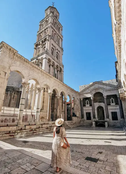Rear view of young woman wearing stylish long dress standing in amazing square inside ancient  Diocletian palace in Split in Croatia.