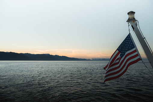 A scenic shot of mountain silhouettes across the sea with the American flag waving on a pole