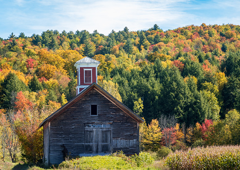Small wooden barn with red cupola set against vibrant Vermont fall colors