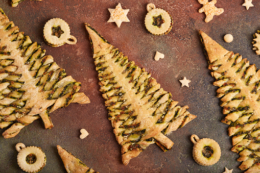 Christmas tree shape puff pastry pie with spinach, garlic and cheese, and puff pastry Linzer Christmas tree toys. Delicious homemade New Year savory baking.