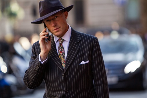 London, United Kingdom – November 09, 2022: A businessman wearing a suit, floral tie, and hat and talking on the phone in London