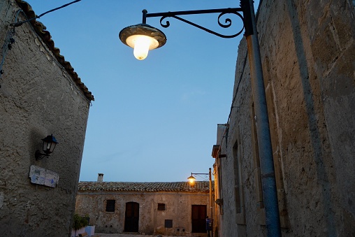 Illuminated vintage street lamps in the streets of Marzamemi, Sicily, at sunset.