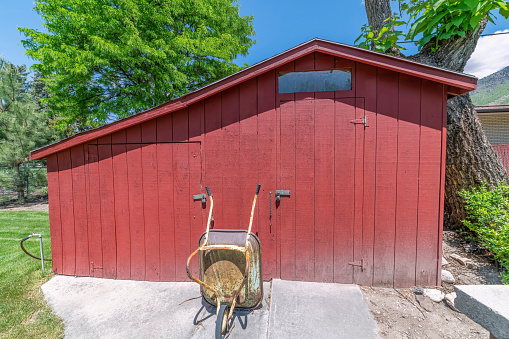 a saltbox red shed with a wheelbarrow in a yard under sunlight
