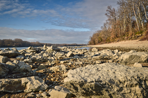 landscape photo of austrian Donau river beach - wild nature reserve area with water side, stones, rocks, trees, clouds and blue sky
