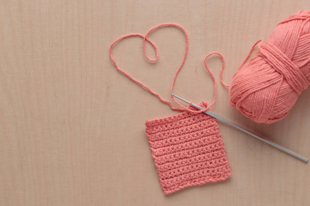 istock Heart Shaped Yarn and Crochet handmade square pattern, pink yarn coil, hook, knitting crocheting top view on a wooden background 1440778180