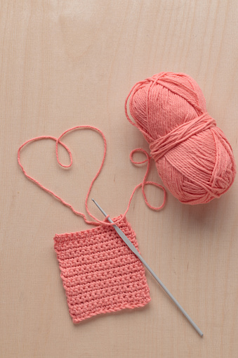 Heart Shaped Yarn and Crochet handmade square pattern, pink yarn coil, hook, knitting crocheting top view on a wooden background with a copyspace