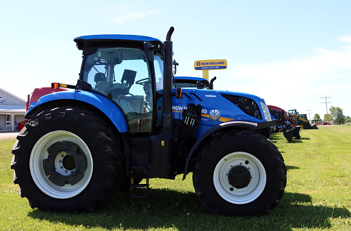 Chesley, Canada – June 06, 2020: Chesley, Ontario / Canada - June 6, 2020: Brand new New Holland blue farm tractor with sign in behind