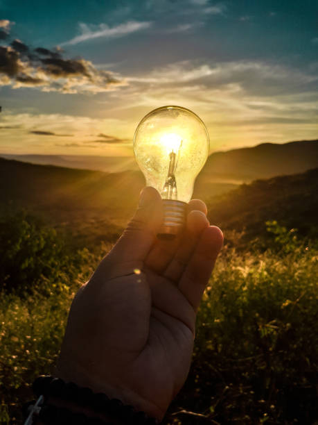 istock Hand holding a light bulb with reflection of a sun during sunset on mountains 1440781185