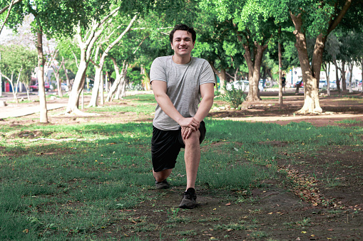 A cheerful Hispanic guy doing a walking lunge in a park