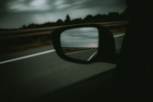 A closeup of the left side-view mirror of a car showing the gray sky behind it on a blurry background