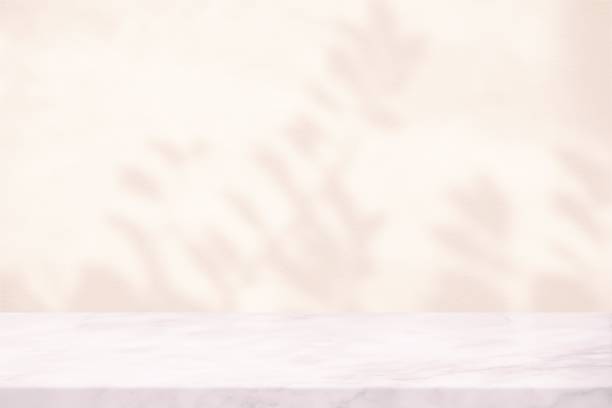 istock White Marble Table with Leaves Shadow on Stucco Wall Texture Background in Set Sail Champagne Tone, Suitable for Product Presentation Backdrop, Display, and Mock up. 1440781695