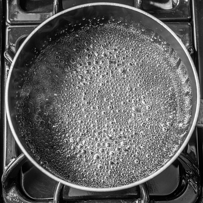 A top view of an empty pan with bubbles and steam rising from it on a black stove