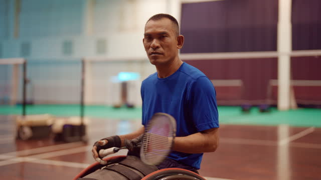 Portrait of Asian man playing and practicing wheelchair badminton at an indoor tennis court.