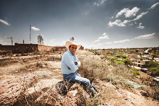 Zacatecas, Mexico – April 01, 2018: A shallow focus of an old Hispanic with a cowboy hat sitting alone at a field in Zacatecas, Mexico