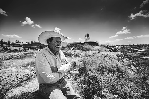 Zacatecas, Mexico – April 01, 2018: A grayscale shot of an old Hispanic with a cowboy hat sitting alone at a field in Zacatecas, Mexico