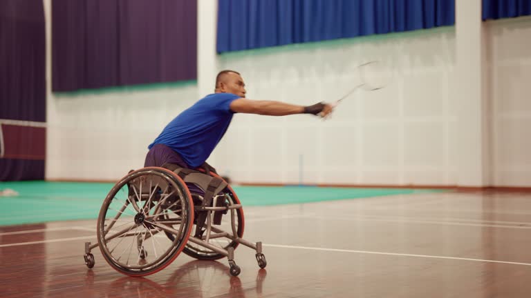 Asian man playing and practicing wheelchair badminton at an indoor tennis court.