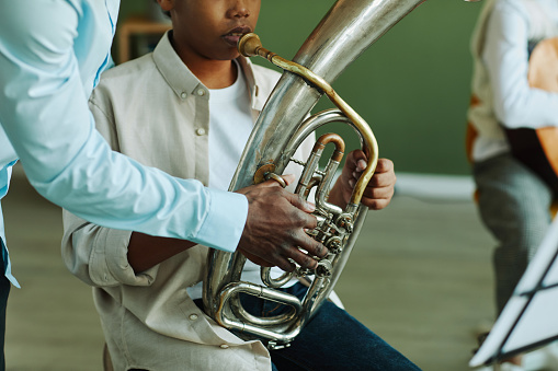 Close-up of hand of young African American music teacher helping pre-teen schoolboy with wind instrument during lesson