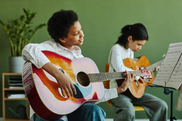 studentessa con la chitarra acustica che guarda la carta con le note sul leggio - guitar child music learning foto e immagini stock