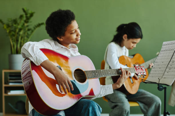 uczennica z gitarą akustyczną patrząca na papier z nutami na stojaku muzycznym - guitar child music learning zdjęcia i obrazy z banku zdjęć