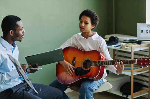 Smiling teenage mixed race boy playing guitar in the kitchen
