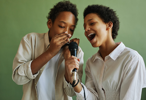 Youthful African American boy and girl performing song together during repetition while playing harmonica and singing in microphone