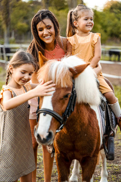 мать с двумя маленькими дочерьми на конном ранчо - horse child pony little girls стоковые фото и изображения
