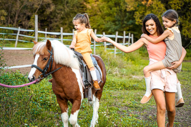 мать с двумя маленькими дочерьми на конном ранчо - horse child pony little girls стоковые фото и изображения