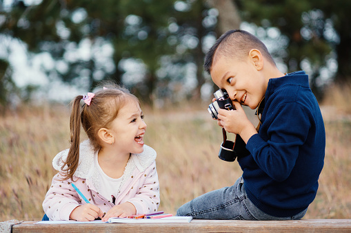 Little boy taking a photo of his smiling sister with a retro camera