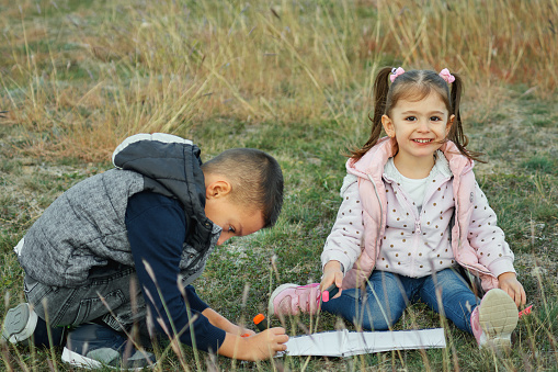 Adorable little girl and boy having fun and drawing in the park