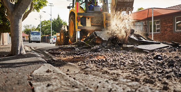 Heavy gigger machine scoop scrapping and removing old asphalt layer during reconstruction of the street in the town