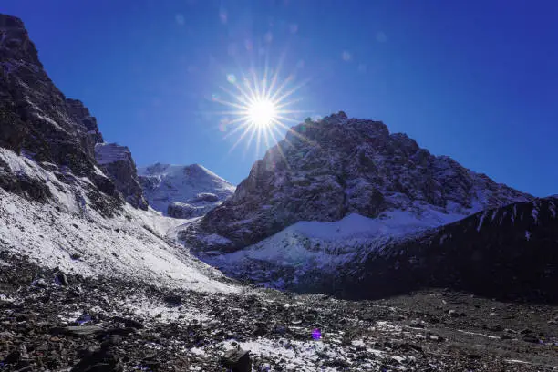 rocky mountain peak with glacier, sunny day landscape, bright starred reflected sun light on clear blue sky