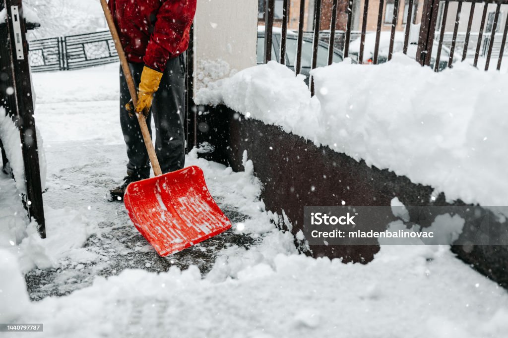 Man with snow shovel Man in red jacket with snow shovel cleans sidewalks and city street in winter. Cloudy winter day. Snow Stock Photo