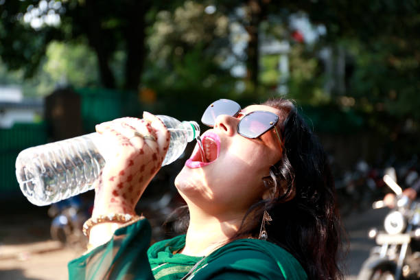 Thirsty women of Indian ethnicity drinking water from water bottle during summer season portrait outdoor in nature.