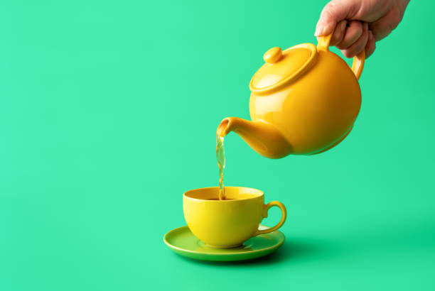 Pouring tea from a teapot in a cup, isolated on a green background stock photo