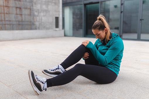 Young woman hurt her knee while working out outdoors. She is in pain.