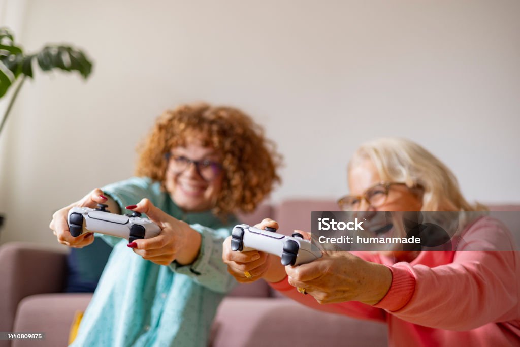 Grandmother and granddaughter competing and cheering while playing playstation Caucasian girl with grandmother playing playstation being focused and having fun Grandparent Stock Photo