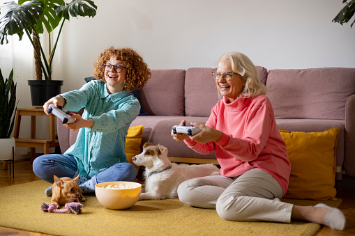 Grandmother enjoying gaming session in living room with her ginger granddaughter and dogs enjoying some family time together