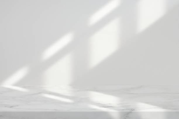 istock Marble Table with White Stucco Wall Texture Background with Light Beam and Shadow from the Window, Suitable for Product Presentation Backdrop, Display, and Mock up. 1440811662