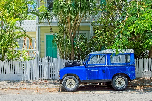 Key West, Florida, USA - May 31, 2019: The quaint pastel colored architecture along a Key West Florida street with a contrasting bright blue Jeep. Typical colorful Key West architecture with white picket fence with contrasting outdoor adventure vehicle parked out front. A travel cityscape scene.