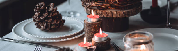 istock Rustic table decor for Christmas or New Year family dinner. Centrepiece with red candle, dry orange, cone, cinnamon, anise. Zero waste eco-friendly home. Cozy atmosphere, dark background. Banner 1440814709