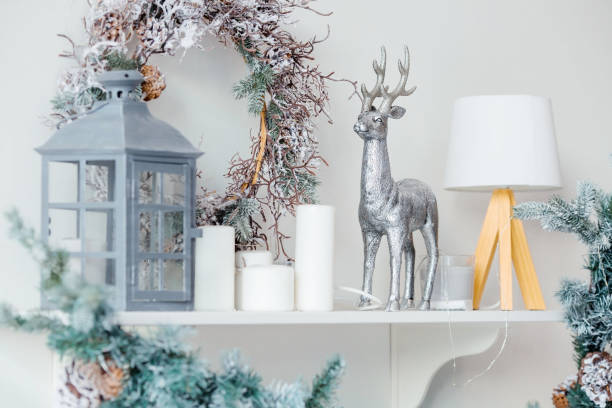 istock Christmas decoration on a shelf in a white interior with Christmas garlands. Flashlight, deer, candles and a Christmas tree. Scandinavian style. Postcard for the new year. 1440818422