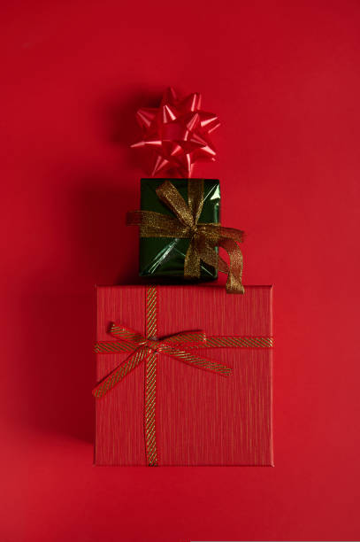 istock Flat lay. Vertical shot gift boxes laid out in shape of Christmas tree, decorated with bow on red background. Still life 1440821544