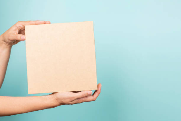 istock Woman hand show brown rectangular cardboard box on light blue background. Mockup parcel box. Packaging, shopping, delivery, present, gift concept 1440823762