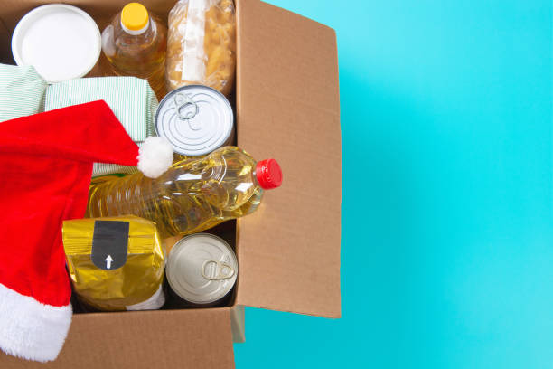 Christmas donation, charity, food bank, help for low income, poor families, migrants, refugees, homeless. Cardboard box full of grocery products and Christmas Santa hat. Top view stock photo