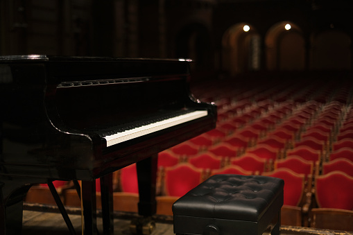 music stage theater with grand piano and white backdrop illuminated with stage light and audience in silhouette