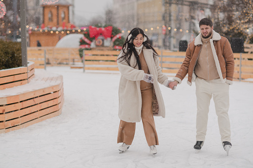 Cheerful loving couple in warm cozy clothes walk outdoors on festive city streets.