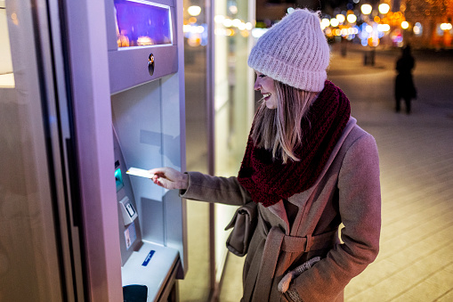 Young woman inserting credit cart to atm at night