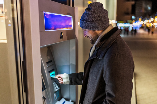 Young man inserting credit cart to atm at night