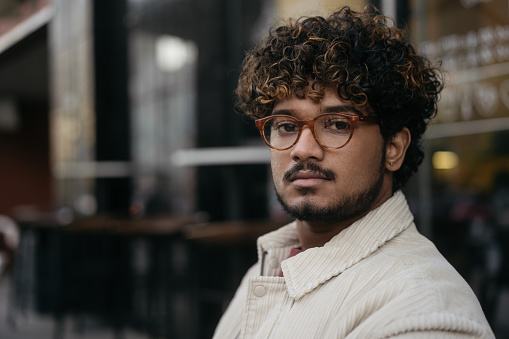 Portrait of pensive Indian man wearing eyeglasses looking at camera on the street, copy space. Vision concept